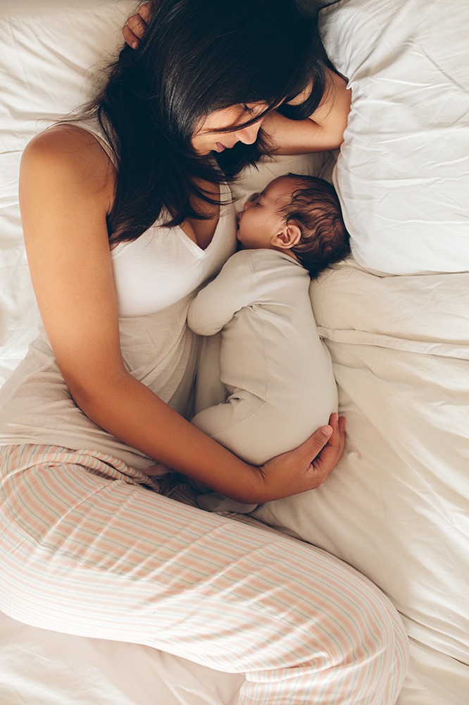 Mother and son sleeping on bed. Young woman with a newborn baby boy in the bed at home.