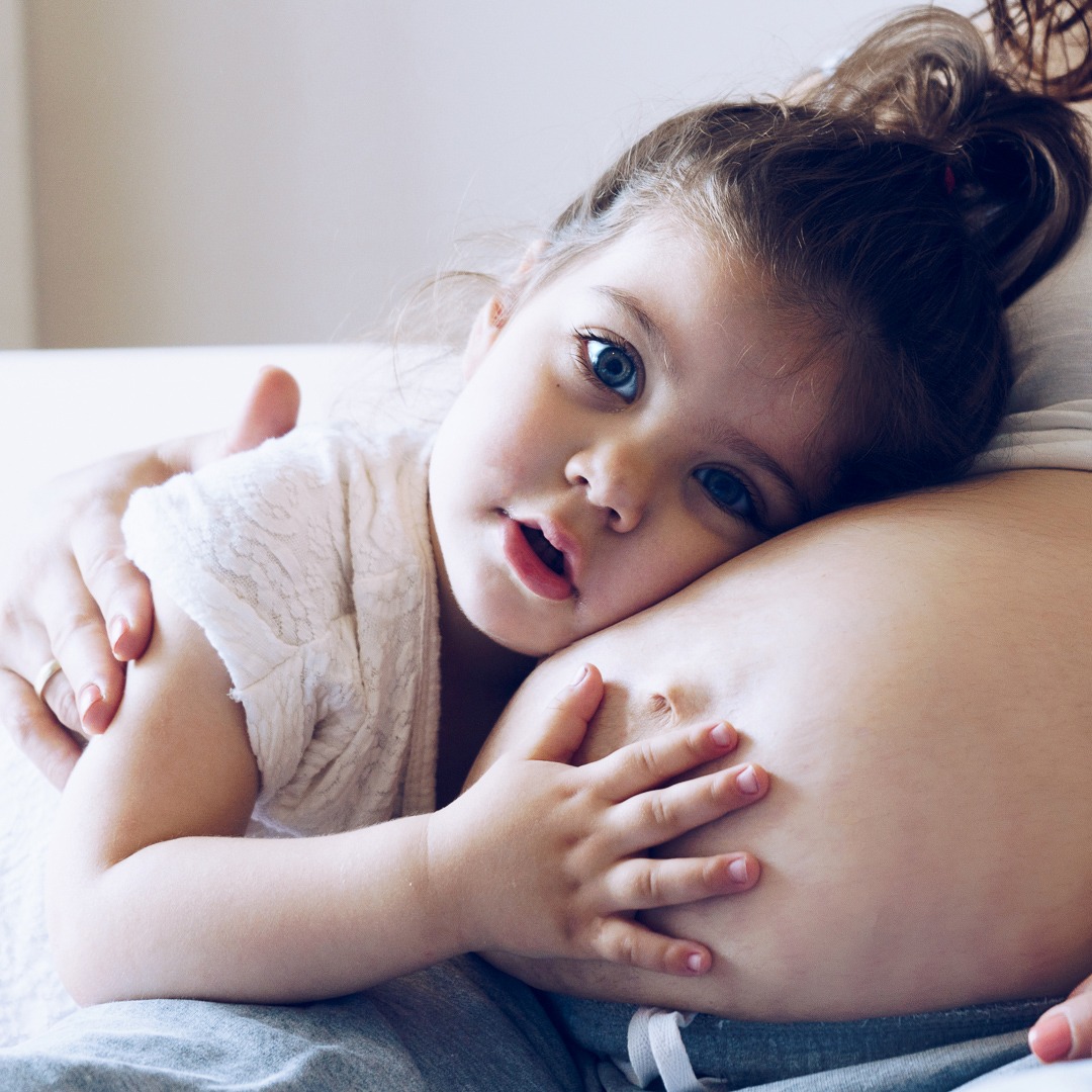 Happy kid girl hugging pregnant mother's belly